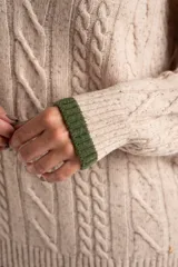 Sweater de lana y nylon color beige jaspeado, con diseño de punto trenzado (cable knit) en todo el cuerpo y mangas. Presenta cuello en V con ribete de dos franjas verdes y puños y bajo con ribete verde liso.