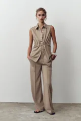 Pantalón de sarga color beige, de tiro medio con cintura elástica en la espalda, bolsillos laterales de plastrón con botón metálico y pierna ancha.