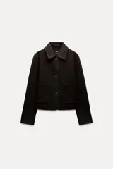 Chaqueta corta negra de cuello solapa y manga larga con puños. Tiene bolsillos de parche en el frente y cierre frontal con botones.