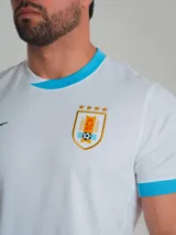 Camiseta de fútbol Nike Stadium de la selección uruguaya, modelo alternativo. Diseño blanco con detalles celestes en cuello y mangas, logo de Nike en negro y escudo de la selección en el pecho.