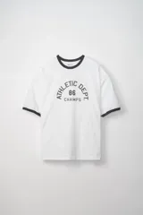 Remera blanca de manga corta con cuello redondo y ribetes en color negro en el cuello y los bordes de las mangas. Estampado frontal en negro con texto de estilo universitario: "ATHLETIC DEPT 86 CHAMPS".