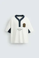 Camiseta blanca de corte relaxed fit, con cuello pico y cierre frontal de botonadura oculta. Presenta mangas cortas y bordados con parche combinados a contraste en delantero y espalda.