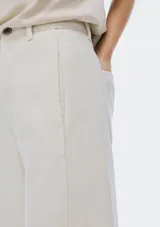 Pantalón de mezclilla color beige claro, de tiro alto y corte ancho (wide leg) que cae recto y amplio hasta el suelo. Presenta cierre frontal y bolsillos laterales.