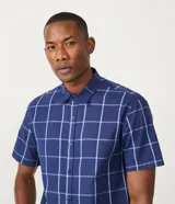 Camisa de manga corta con estampado de cuadros azules y blancos, cuello camisero y abotonadura frontal.