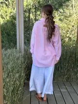 Camisa holgada a rayas verticales color beige y blanco, con cuello clásico, manga larga, bolsillo en el pecho y cierre frontal con botones nacarados.