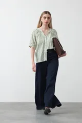 Camisa de viscosa con estampado de pequeños lunares verdes sobre fondo blanco o crema. Presenta escote en V con botones frontales y mangas cortas abullonadas con elástico en el puño.