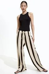 Pantalón de punto color crema con rayas verticales negras y marrones, de corte holgado y tiro alto, con cintura elástica y cordón ajustable.