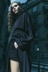 Parka larga negra con capucha ajustable con cordones, mangas largas con puños elásticos, bolsillos laterales y de plastrón en el pecho, bajo ajustable con cordón elástico y cierre frontal con cremallera metálica.