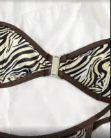 Conjunto de bikini con estampado de cebra en tonos beige y negro, con ribetes marrones. Incluye corpiño bandeau con hebilla metálica central y tanga de tiro bajo.