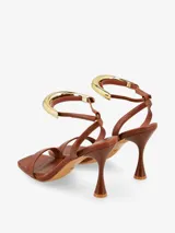Sandalias de tacón negras con tira delgada sobre los dedos y pulsera tobillera con adorno tubular plateado.