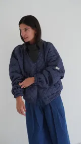 Campera puffer azul marino con diseño acolchado de rombos, cuello de cuero sintético negro, mangas largas abullonadas con puños elásticos y cierre frontal con cremallera.