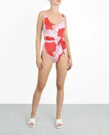 Traje de baño enterizo con estampado de flores rojas y hojas color crema sobre fondo lila. Presenta corte alto en la pierna y cinturón lila con lazada lateral.