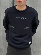 Buzo negro de corte holgado con cuello redondo y puños acanalados. Estampado frontal con la palabra "OSTEN" y la frase "NOT WHERE YOU'RE FROM A MINDSET OF BECOMING" en color blanco.
