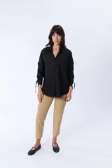 Camisa negra de manga larga con cuello clásico y cierre frontal con botones. Las mangas tienen frunces y lazos para ajustar el largo.