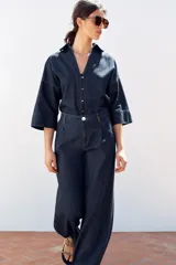 Pantalón de jean azul oscuro, corte wide leg, tiro alto con pinzas delanteras, bolsillos laterales y cierre frontal con cremallera y botón.