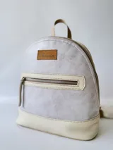 Mochila pequeña de cuero color gris claro y beige, con cierre superior y bolsillo frontal con cierre. Tiene asa de mano y correas ajustables para los hombros.