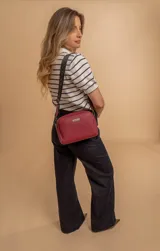 Bandolera pequeña de textura símil cuero color caramelo/marrón, con dos compartimentos principales con cierre. Correa ancha ajustable de tela negra con inscripción en relieve.