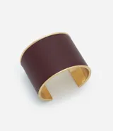 Pulsera tipo brazalete rígido de abertura, con exterior de cuero sintético color borgoña y bordes y base metálica en tono dorado.