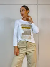 Remera blanca con diseño gráfico en dorado, de mangas largas y ajuste ceñido al cuerpo.