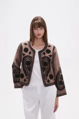 Chaqueta corta de algodón color marrón topo, sin cuello, con bordados florales y de estilo paisley en negro. Presenta un borde festoneado y mangas largas.