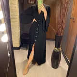 Vestido largo negro con botones frontales, abertura lateral y mangas anchas.