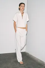 Chaqueta corta negra de cuello solapa y manga corta. Cierre frontal con cremallera metálica y bolsillos de ojal. Zara Woman Collection.