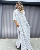 Vestido largo tipo camisero con estampado de rayas verticales en color blanco y celeste. Presenta cuello camisero, cierre frontal con botones, mangas largas y tajos laterales en el ruedo.