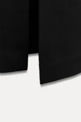 Vestido midi negro de escote pico y manga larga con hombreras. Tiene falsos bolsillos de vivo en el delantero y cierre en la espalda con cremallera oculta.