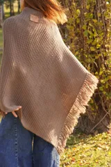 Poncho tejido en lana merino color marrón topo, con cuello redondo y terminación con flecos.