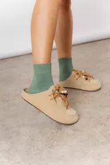 Zueco de cuero gamuzado color beige, con cordones decorativos con cuentas y piezas envueltas en cuero. Tiene plantilla acolchada y base liviana.