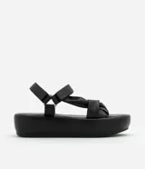 Sandalia flatform negra de material sintético, con punta redonda y tiras torcidas.