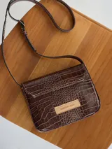 Cartera bandolera marrón con textura tipo piel de cocodrilo, correa larga ajustable y cierre con solapa.