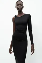 Vestido midi negro de punto, con cuello asimétrico, manga sisa, aplique metálico dorado en el hombro y drapeado lateral.