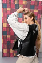 Chaleco corto negro de cuero con solapas y bolsillos frontales.