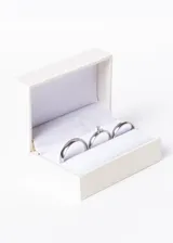 Set de tres anillos de acero quirúrgico plateado. Incluye dos alianzas lisas de 4mm y un cintillo con un cristal engarzado. Se presenta en estuche blanco.