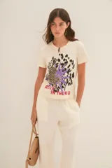 Remera color crudo de algodón con estampado de leopardo, hojas de palma y texto 'Rock in the wind'.