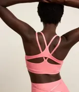 Top deportivo con copas removibles, confeccionado en microfibra color salmón. Presenta tiras elásticas cruzadas en la espalda con logo estampado.