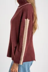 Sweater negro de tejido grueso con cuello alto acanalado. Presenta una franja decorativa en las mangas y el cuello en hilo marrón con brillo (lurex).