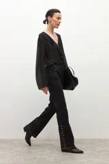 Jean negro de tiro medio, corte bootcut, con tachas metálicas plateadas decorando los laterales de las piernas y el ruedo.