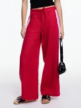 Pantalón de lino rojo con elástico en la cintura, tiro medio y calce relajado. Lleva tiras en color lila aplicadas a los laterales, que quedan sueltas en la parte inferior y pueden anudarse para jugar con el estilo.