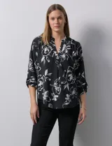 Blusa de gasa estampada con flores blancas sobre fondo negro, marca Floral & Ivy. Tiene cuello a la base con escote en V y mangas tres cuartos regulables con presilla y botón.