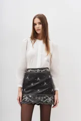 Minifalda negra de cuero ovino con apliques de lentejuelas y bordados plateados en la cintura y el ruedo.