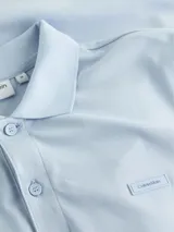 Chomba celeste de algodón orgánico, corte slim, cuello clásico con dos botones, manga corta, puños de punto, aberturas laterales y logo bordado en el pecho.