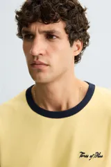 Camiseta amarilla de corte regular fit, cuello redondo y manga corta. Tiene un bordado frontal de texto en color azul marino. Acabados con rib a contraste en cuello y mangas.