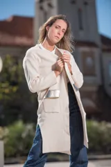 Saco largo color crudo, con cuello redondo, bolsillos frontales con apliques de cuero plateado y mangas largas.