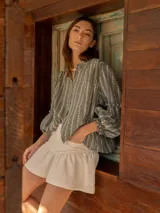 Camisa verde con rayas verticales blancas y bordado de flores. Tiene cuello mao, mangas largas abullonadas con puños elásticos y cierre frontal con botones de nácar.
