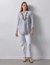 Blusa de gasa bambula a rayas verticales celestes y blancas, con cuello a la base, escote en V con botones y bordado floral negro. Mangas largas regulables con presilla y botón.