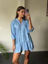 Vestido corto blanco con escote en V, mangas 3/4 con detalle de calado y volados en el ruedo. Cierre frontal con botones.