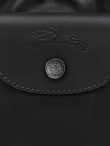 Bolso pequeño tipo cubo (bucket bag) de cuero negro, con cordón ajustable en la parte superior y solapa con broche a presión. Se lleva cruzado con una correa fina y ajustable.