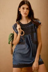 Vestido corto azul denim con bordados en hilo negro en escote, mangas y ruedo. Corte amplio y bolsillos laterales ocultos.